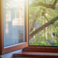 Geöffnetes Fenster mit dunklem Holzrahmen mit Blick in den Garten