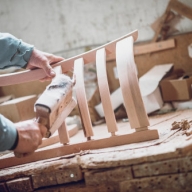 Hände eines Tischlers schleifen die Lehne eines Holzstuhles ab