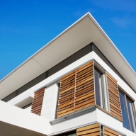 Blick zum Dach eines Einfamilienhauses. Außen an den Fenstern befinden sich Holzjalousien.